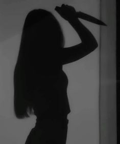 the silhouette of a woman holding a knife up to her head in front of a window