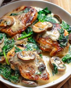 a white bowl filled with chicken, mushrooms and spinach on top of a wooden table