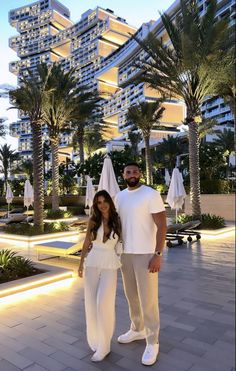 a man and woman standing next to each other in front of palm trees