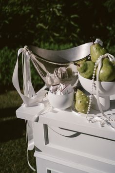 some green apples are sitting in bowls on a white table cloth with pearls around them