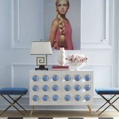 a white sideboard with blue circles on it in front of a painting and two chairs