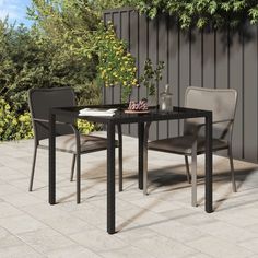 an outdoor dining table with four chairs and an umbrella over it, surrounded by greenery