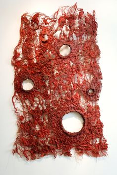 a piece of art that looks like red yarn with holes in the middle, on a white surface