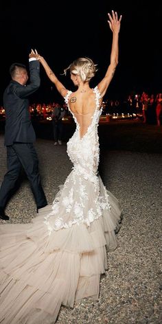 a woman in a wedding dress dancing with her arm raised up to the sky while a man in a black suit stands behind her