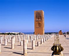 a very tall clock tower towering over a city filled with columns and pillars in front of the ocean