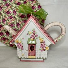 a teapot shaped like a house with flowers on it and a green bow around the top