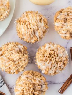 several muffins with icing and cinnamon sticks on a marble surface next to an orange cupcake