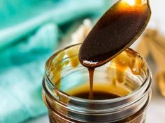 a spoon full of brown liquid being poured into a mason jar with honey in it