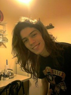 a young man with long hair standing in front of a counter smiling at the camera