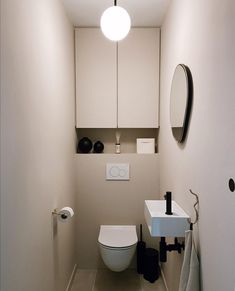 a white toilet sitting next to a sink in a bathroom under a round light fixture