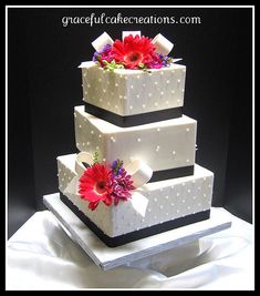 three tiered wedding cake with flowers on each layer and polka dot design, sitting on top of a white table cloth