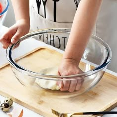 a person is kneading dough into a bowl on a cutting board with utensils