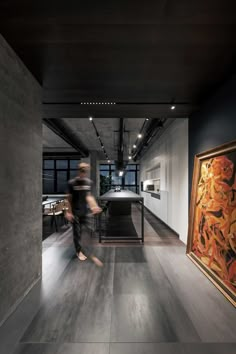 a person walking through a room next to a painting on the wall and an open kitchen area