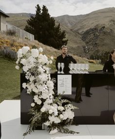 a man and woman standing behind a bar with flowers on it