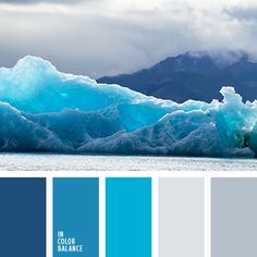 an iceberg with blue hues in the water and mountains in the back ground