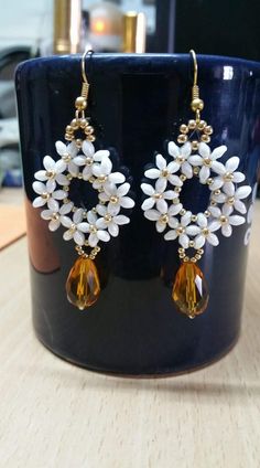 a pair of white and yellow earrings sitting on top of a wooden table next to a cup