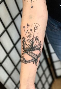 a woman's arm with a book and flowers tattoo on the left inner forearm