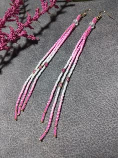 pink and white seed beaded earrings on grey surface next to purple flower with green leaf