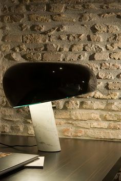 a desk lamp sitting on top of a wooden table next to a brick wall and laptop computer