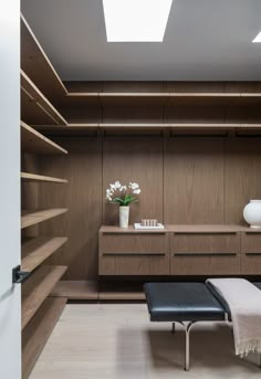 a room with shelves and a bench next to a vase filled with flowers on top of it