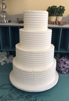 a three tiered white cake sitting on top of a table next to purple flowers