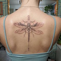 the back of a woman's shoulder with a dragonfly tattoo on her upper arm