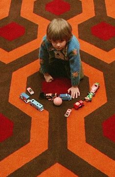 a young boy playing with toy cars on the floor in front of a carpet pattern