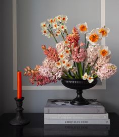 a vase filled with lots of flowers sitting on top of a book next to a candle