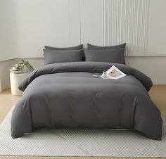 a bed with grey sheets and pillows on top of a white rug next to a window