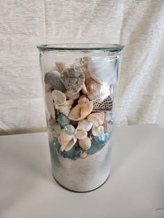 a glass jar filled with sea shells on top of a white tablecloth covered wall