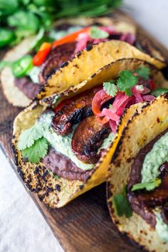 three tacos with meat and vegetables on a wooden cutting board next to green peppers