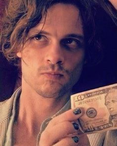 a man holding up a dollar bill in his right hand and looking at the camera