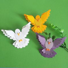 three different colored paper birds on a green surface