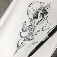 a black and white drawing of a mermaid on paper with a pen next to it