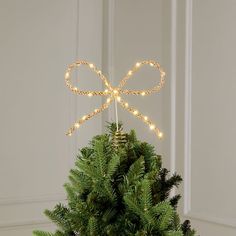 a small christmas tree with lights on it and a bow hanging from the top, in front of a white wall