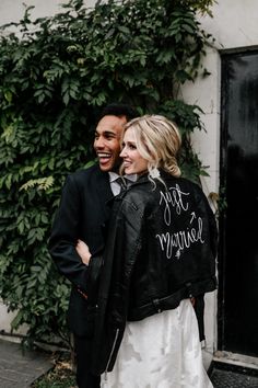 a man and woman standing next to each other in front of a green plant covered wall