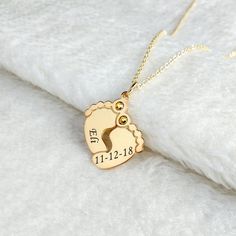 a gold plated necklace with a child's feet and name on it, sitting on a white surface