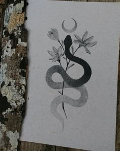 a piece of paper with a snake and flowers on it next to a tree trunk