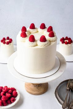 a white cake with raspberries on top and other desserts in the background