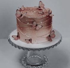 a pink cake with butterflies on it sitting on top of a white plate and silver platter