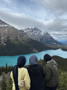 three people standing on top of a mountain looking at a lake