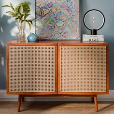 an art piece on top of a wooden cabinet in front of a painting and plant