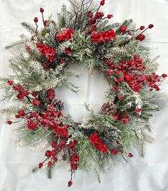 a christmas wreath with red berries, pine cones and greenery is displayed on a white sheet