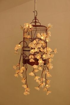 a birdcage with white flowers hanging from it's sides and lights in the middle