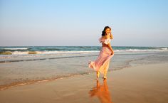 a woman in a pink dress walking on the beach