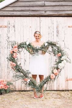 a woman standing in front of a wooden wall holding a heart shaped wreath with flowers