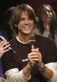 a smiling man holding a microphone in front of two other people and talking on the phone