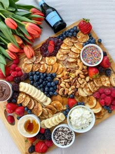 Mini panckae board surrouned by fresh fruit, nuts, whipped cream and nutella next to a boquet of orange tulips and champange Mini Pancake Brunch, Pancake Grazing Board, Mini Pancake Board, Mini Breakfast Charcuterie Board, Mini Pancake Charcuterie Board, Pancake Breakfast Board, Brunch Food For Party, Fall Brunch Charcuterie Board, Kid Brunch Ideas