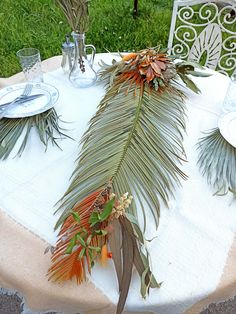 the table is set with plates and silverware, palm fronds on it