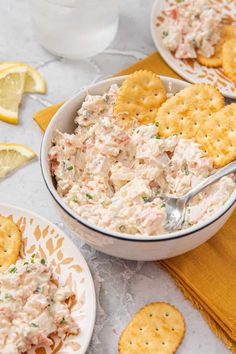 a bowl full of crab salad with crackers and lemon wedges on the side